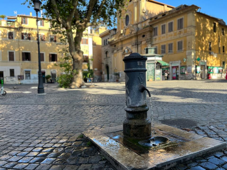 A cylindrical drinking fountain in Rome atop a square stone and cobblestones
