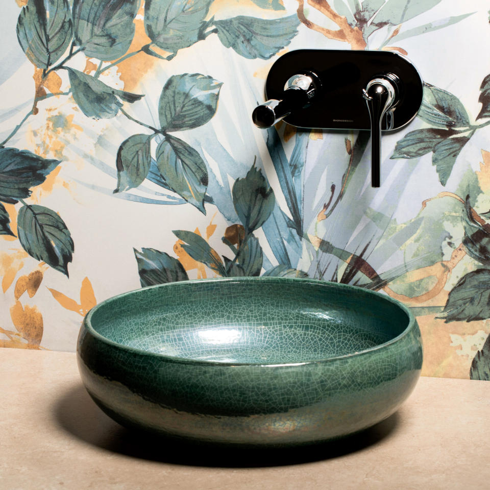 Round green glazed countertop basin next to a wall with botanical design