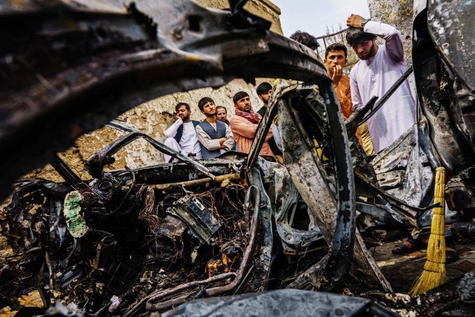 Relatives of the Ahmadi family gather around an incinerated vehicle hit earlier by a drone strike