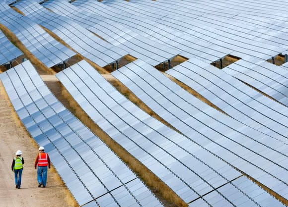 Two solar technicians walk along a utility-scale solar project.