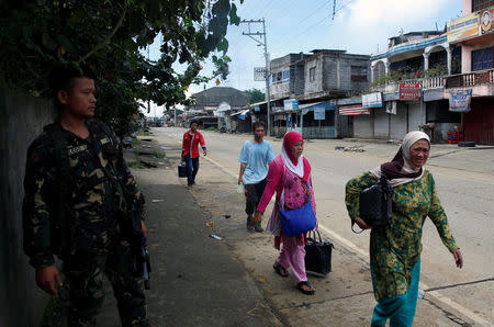 Residents walk past soldiers in Marawi City as fighting rages between government soldiers and the Maute militant group, in southern Philippines May 27, 2017. REUTERS/Erik De Castro