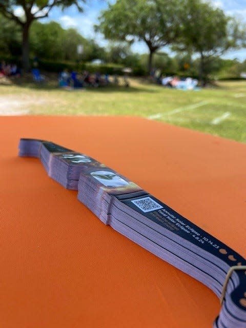 While people take cover from the sun in the shade awaiting the start of the solar eclipse, special eclipse viewing glasses wait to be distributed.