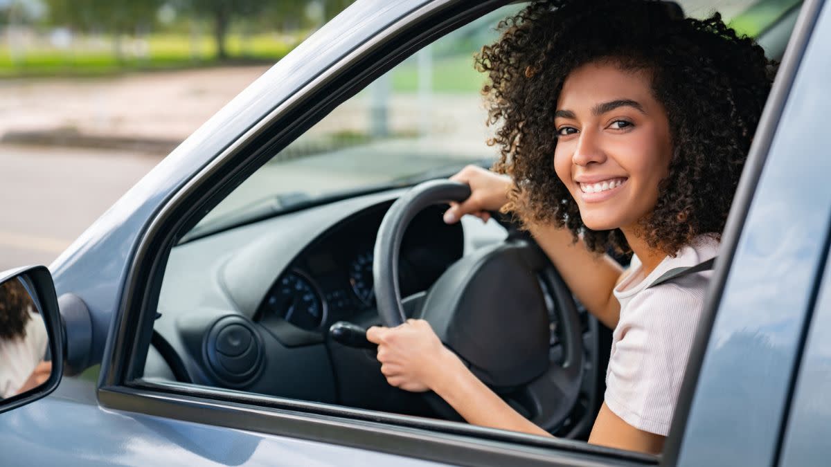 woman smiling while holding steering wheel of a car