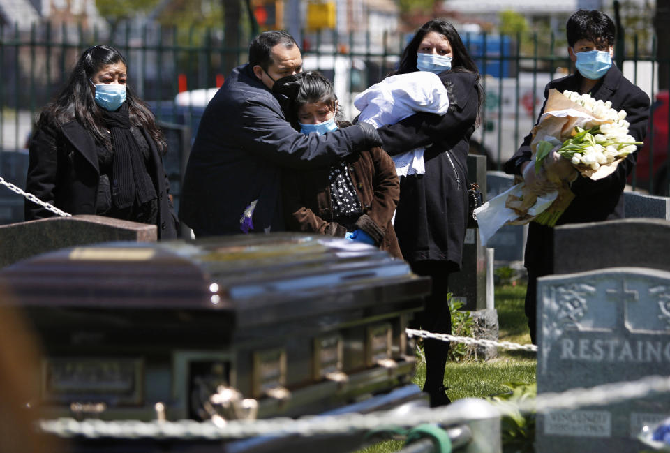 In this May 12, 2020 photo, the Rev. Joseph Dutan comforts his niece, Valerie Dutan, at the funeral of his father, Manuel Dutan, at St. John's Cemetery in the Queens borough of New York. Within one month, Dutan experienced the loss of his father and a fellow cleric, whom he considered a mentor. (AP Photo/Jessie Wardarski)