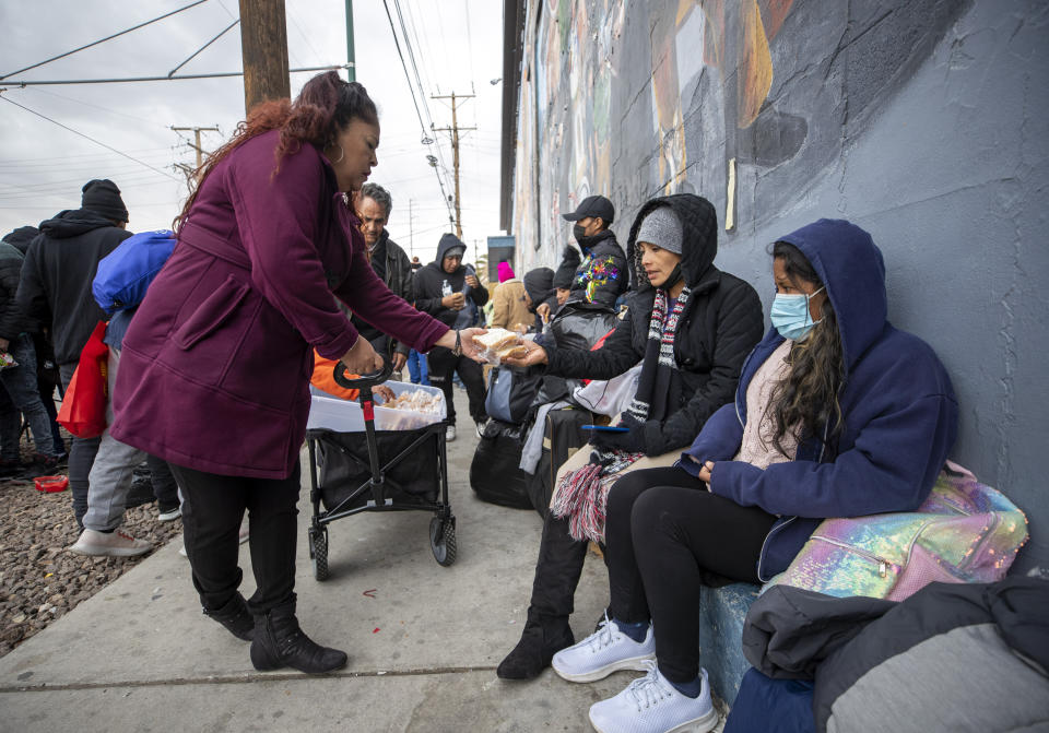 A resident distributes homemade sandwiches to migrants camping on a street in downtown El Paso, Texas, Sunday, Dec. 18, 2022. Texas border cities were preparing Sunday for a surge of as many as 5,000 new migrants a day across the U.S.-Mexico border as pandemic-era immigration restrictions expire this week, setting in motion plans for providing emergency housing, food and other essentials. (AP Photo/Andres Leighton)