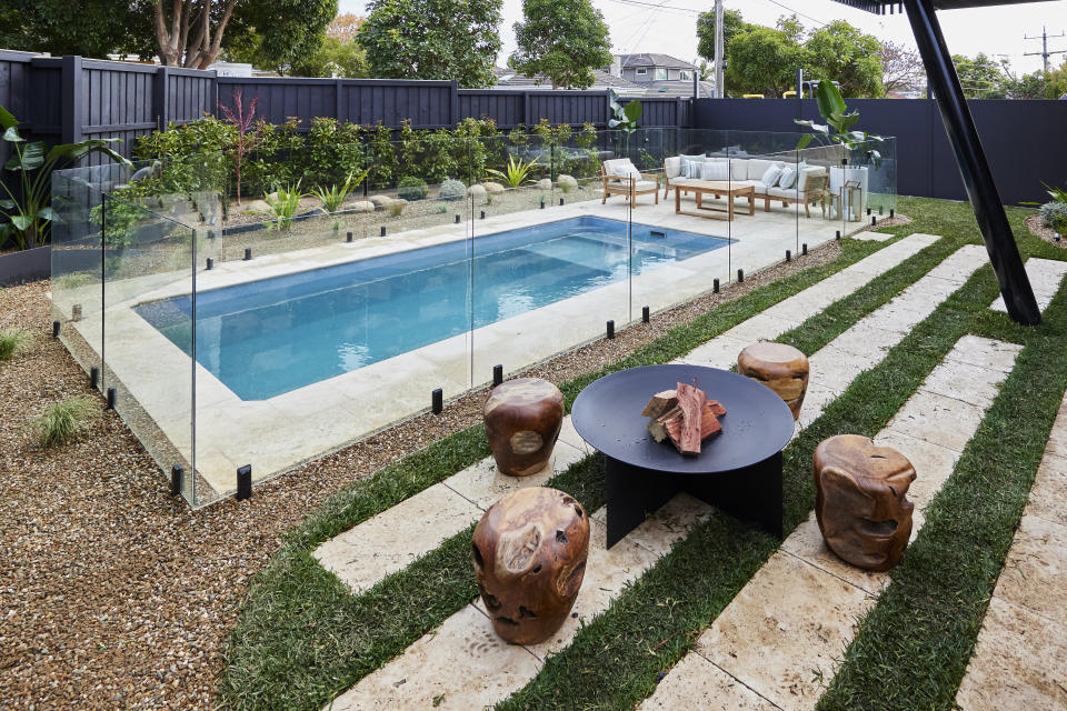 A shot of the pool and the firepit with four wooden seats around it. 