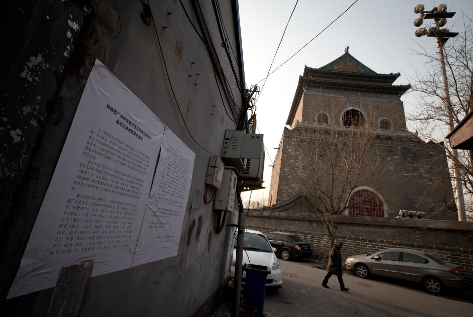 In this photo taken on Dec. 26, 2012, a woman walks past a Hutong house with a demolition notice placed on the wall, near the historical Drum and Bell Tower, right in the background, in Beijing. The district government wants to demolish scuffed courtyard homes, move their occupants to bigger apartments farther from the city center and redevelop a square in 18th century Qing Dynasty fashion. (AP Photo/Andy Wong)