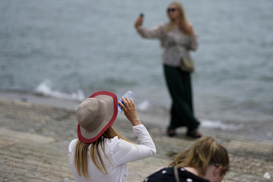 A woman drinks water while another takes a selfie by the water on the Tagus river bank at Lisbon's Comercio square, Monday, July 11, 2022. Temperatures in Portugal have dropped in the last couple days bringing some respite from a heatwave but are expected to rise again Tuesday and reach 46 degrees Celsius (115 Fahrenheit) in some parts of the country by Thursday. (AP Photo/Armando Franca)