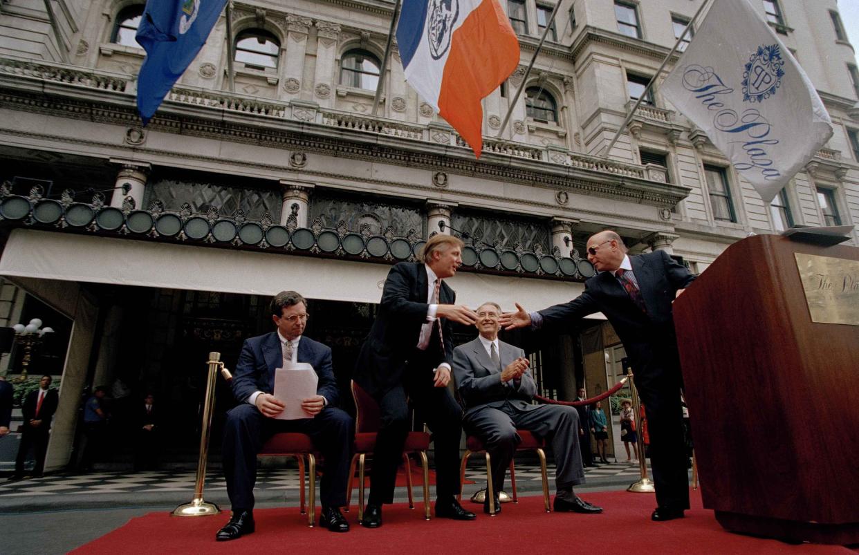 Donald Trump, second from left and former owner of the Plaza Hotel, reaches to shake the hand of Robert Small, right, CEO of Fairmont Hotel Management at a flag raising ceremony at the Plaza Hotel, on July 28, 1995.