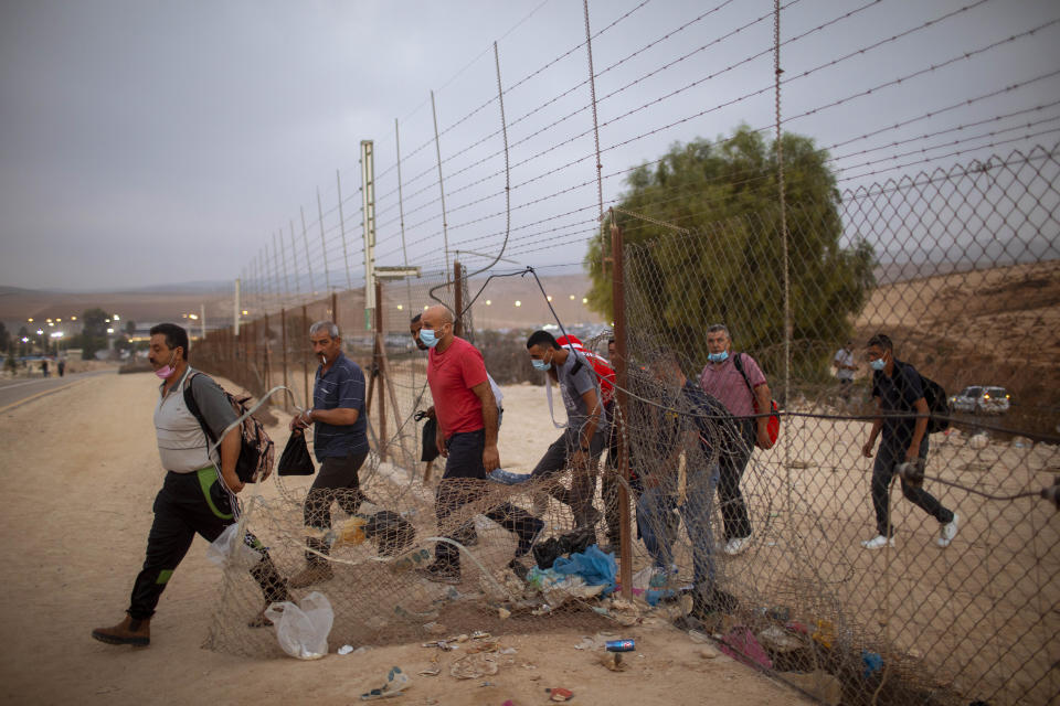 FILE - In this Sunday, Sept. 6, 2020 file photo, Palestinian laborers some wearing protective face masks amid concerns over the country's coronavirus outbreak, cross illegally into Israel from the West Bank through an opening in a fence, south of the West Bank town of Hebron. Israel's premier human rights group has begun describing both Israel and its control of the Palestinian territories as a single "apartheid" regime, using an explosive term that the Israeli government and its supporters vehemently reject. (AP Photo/Oded Balilty, File)