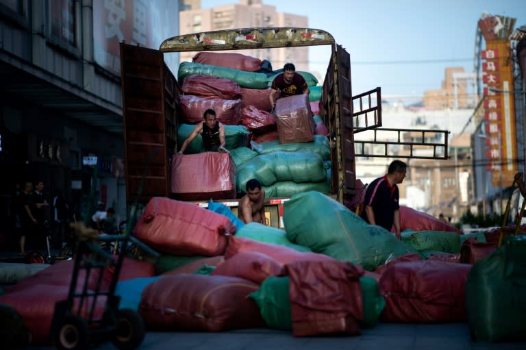 Workers unload bags with clothes from a truck in front of a wholesale clothing market in Shanghai