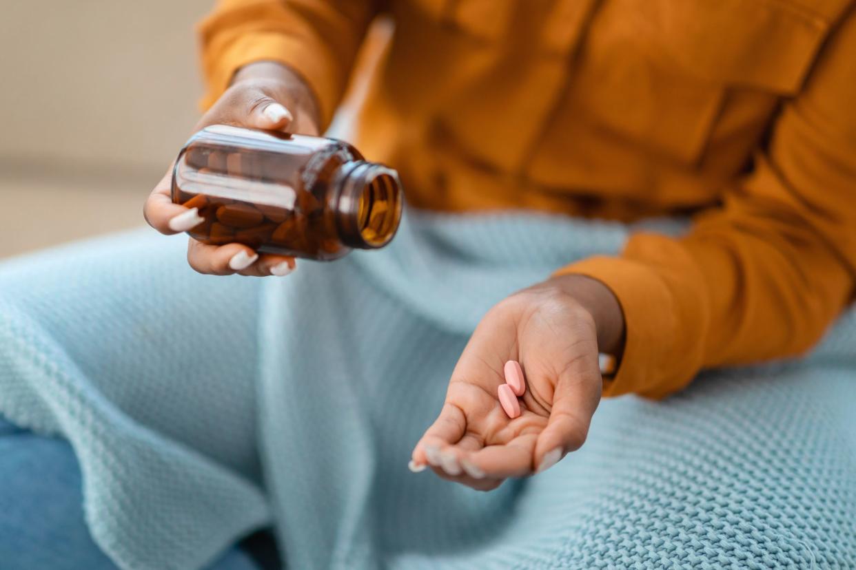 Close-up of african american woman's hands as she pours pink pills from a brown medicine bottle, possibly indicating health management, medication routine, or vitamin supplementation