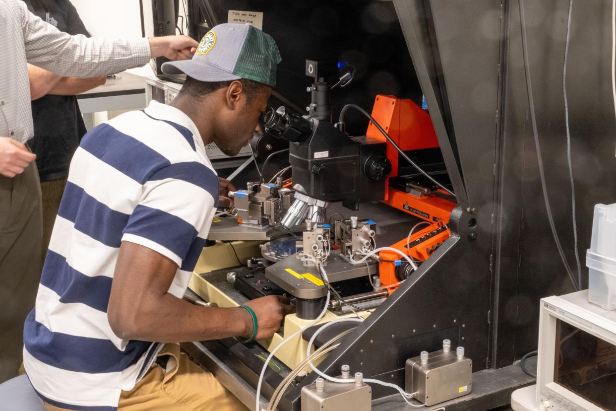 Senior electrical engineering student Couby Ouattara inspects a semiconductor chip using a probe station and parameter analyzers donated to UVM's Device Characterization lab by GlobalFoundries.