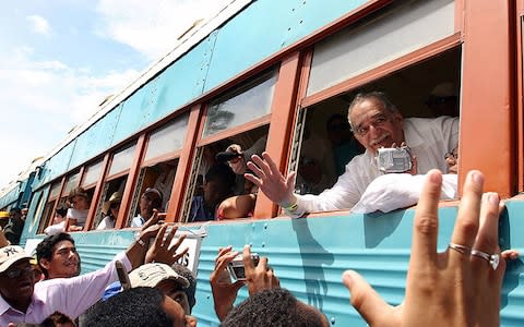 Gabriel García Márquez, pictured far right, leaning out of the window of the train upon arrival at his hometown Aracataca in 2007 - Credit: Getty