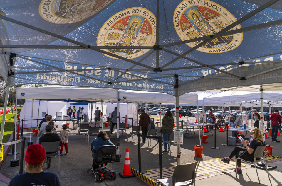 FILE - In this March 4, 2021, file photo, people wait under tents for their turn to be vaccinated at the St. John's Well Child and Family Center COVID-19 vaccination site at the East Los Angeles Civic Center in Los Angeles. California's two largest counties, Los Angeles and San Diego, have signed on to administer vaccine under a centralized system operated by insurer Blue Shield, greatly advancing Gov. Gavin Newsom's vision of a uniform COVID-19 vaccine network despite widespread pushback from local health offices. (AP Photo/Damian Dovarganes, File)