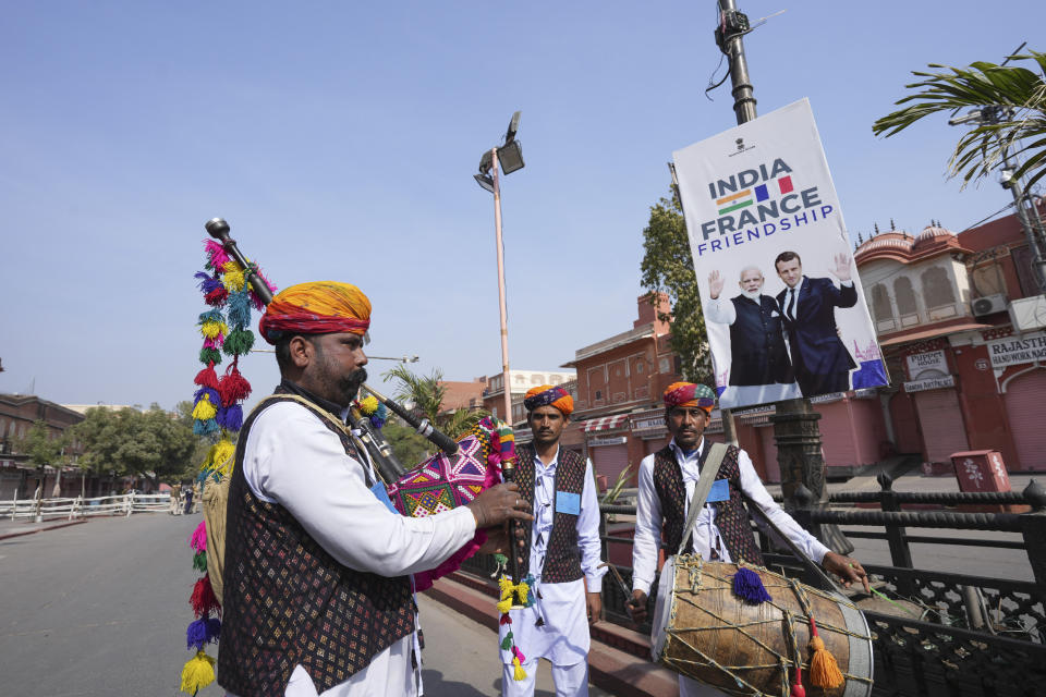 Indian folk artists stand next to a poster showing French President Emmanuel Macron with Indian Prime Minister Narendra Modi erected ahead of Macron's arrival in Jaipur, Rajasthan, India, Thursday, Jan.25, 2024. Macron will be the chief guest at India's annual republic day parade in New Delhi on Friday. (AP Photo/Deepak Sharma)