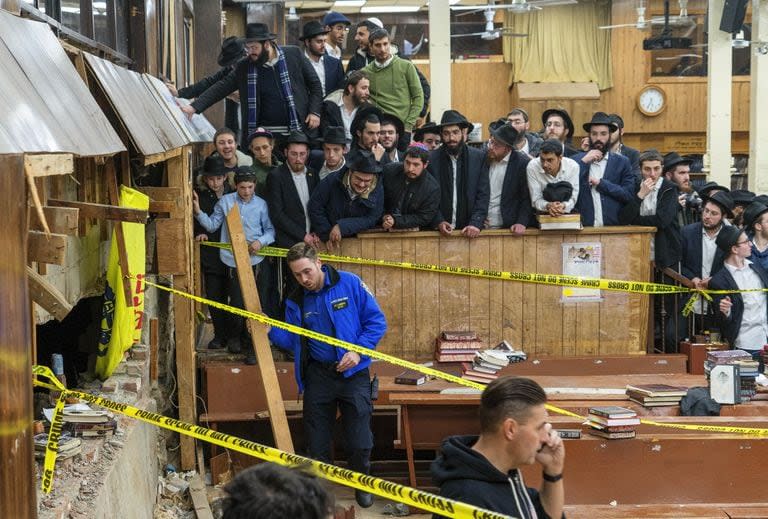 Estudiantes judíos jasídicos observan mientras las fuerzas del orden establecen un perímetro alrededor de una pared perforada en la sinagoga que condujo a un túnel excavado por estudiantes, el lunes 8 de enero de 2024, en Nueva York.