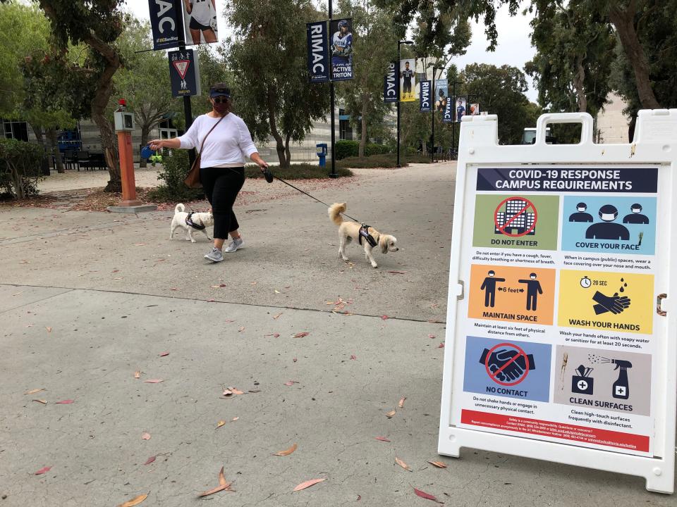 Marina Bruce, an assistant director of admissions at the University of California-San Diego, takes her dogs for a walk amid signs outlining COVID-19 precautions.
