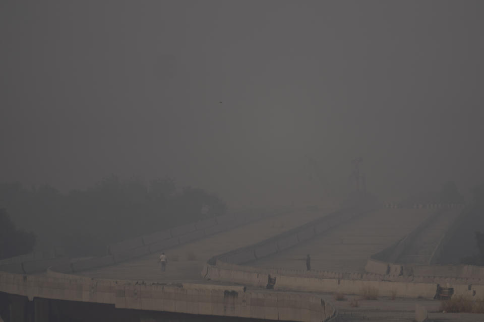 People jog on an under construction flyover amid smog in New Delhi, India, Tuesday, Nov. 7, 2023. Masks are back on the streets as residents of the capital city grapple with the annual surge in air pollution that has engulfed the region. (AP Photo/Altaf Qadri)