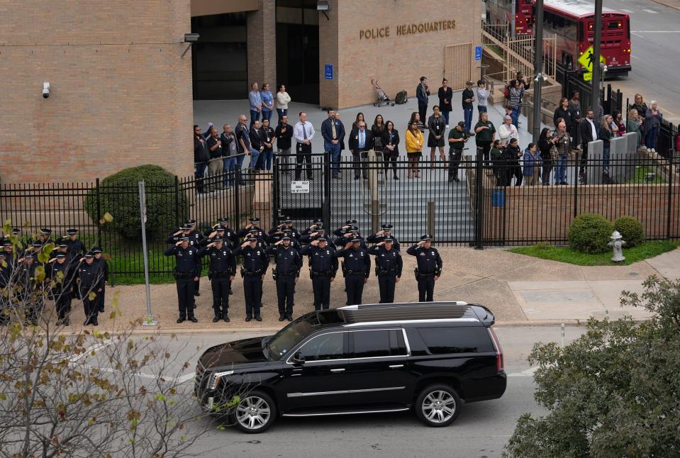 Police officers salute outside the Austin Police Department's headquarters as Jorge Pastore's funeral procession passes on its way to Circuit of the Americas.