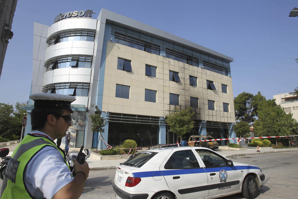 A policeman stands in front of Microsoft's offices in northern Athens, Wednesday, June 27, 2012. Assailants attacked the offices of Microsoft early Wednesday, driving a van through the front doors and setting off an incendiary device that burned the building entrance, police said. (AP Photo/Thanassis Stavrakis)