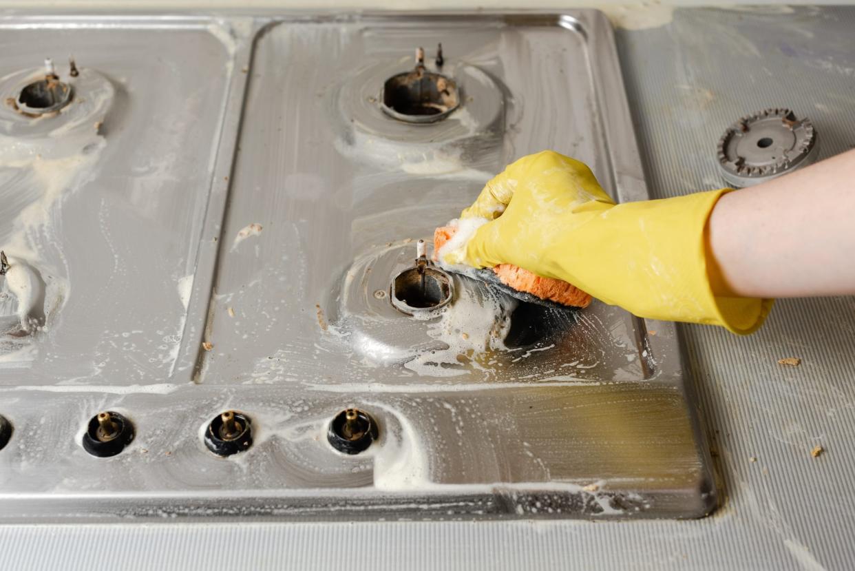 Hand in yellow rubber glove wash gas stove burner