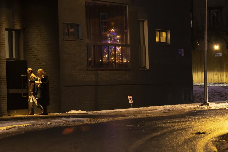 A couple walk past an apartment building windows with a Christmas tree sparkling with festive lights in Tallinn, Estonia, on Friday, Dec. 22, 2023. In Estonia, as in many parts of the world, trees covered with lights brighten up homes and town squares during the Winter Solstice and Christmas festivities afterwards. (AP Photo/Pavel Golovkin)