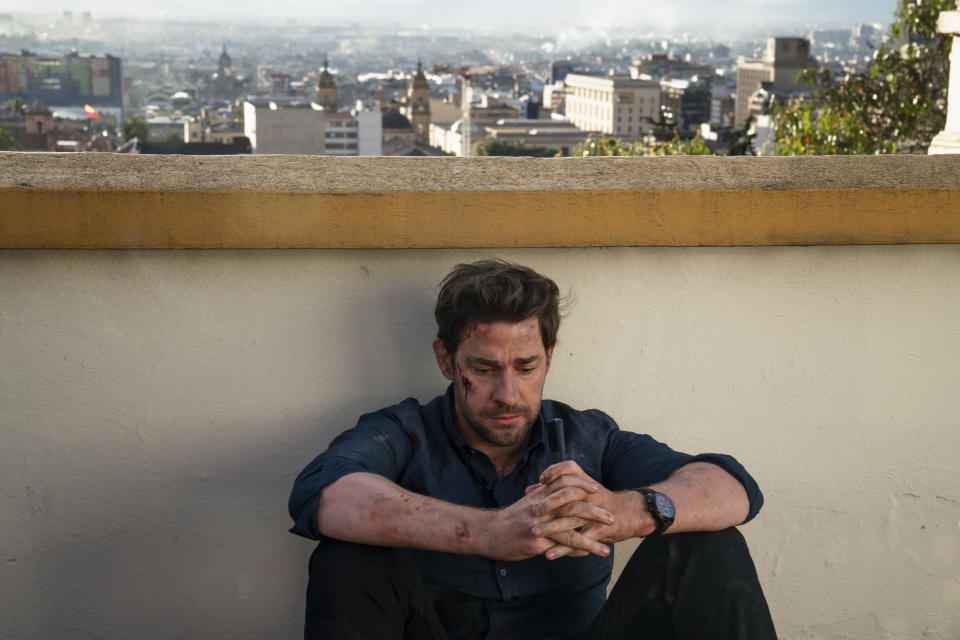 John Krasinski as Jack Ryan sits with his arms, with hands clasped, on his raised knees