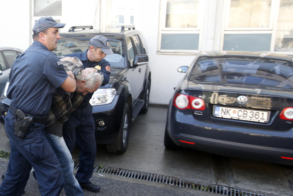 FILE - In this Sunday Oct. 16, 2016 file photo, Montenegrin police officers escort a man suspected of planning armed attacks after the parliamentary vote in Podgorica, Montenegro. A court in Montenegro has sentenced 13 people, including two Russian secret service operatives, to up to 15 years in prison after they were found guilty of plotting to overthrow the Balkan country's government and prevent it from joining NATO. (AP Photo/Darko Vojinovic, File)