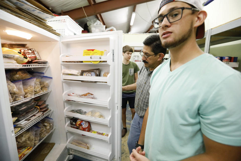 In this Thursday, Aug. 8, 2019 photo, while his father, Pastor Hugo Villegas inspects the freezer, Pablo Villegas, right, says the pantry at the Carlisle Crisis Center in Forest, Miss., has a limited amount of perishable foods, courtesy of the immediate community, as well as contributions from individuals as far away as Jackson, and help from some social agencies and civic groups. The center, a ministry of Scott County Baptist Association, says they will need more food items to help out the families affected by the fallout of Wednesday's raid by U.S. immigration officials at poultry plants Koch Foods and PH Foods in neighboring Morton. The raids were part of a large-scale operation targeting owners as well as undocumented employees. (AP Photo/Rogelio V. Solis)