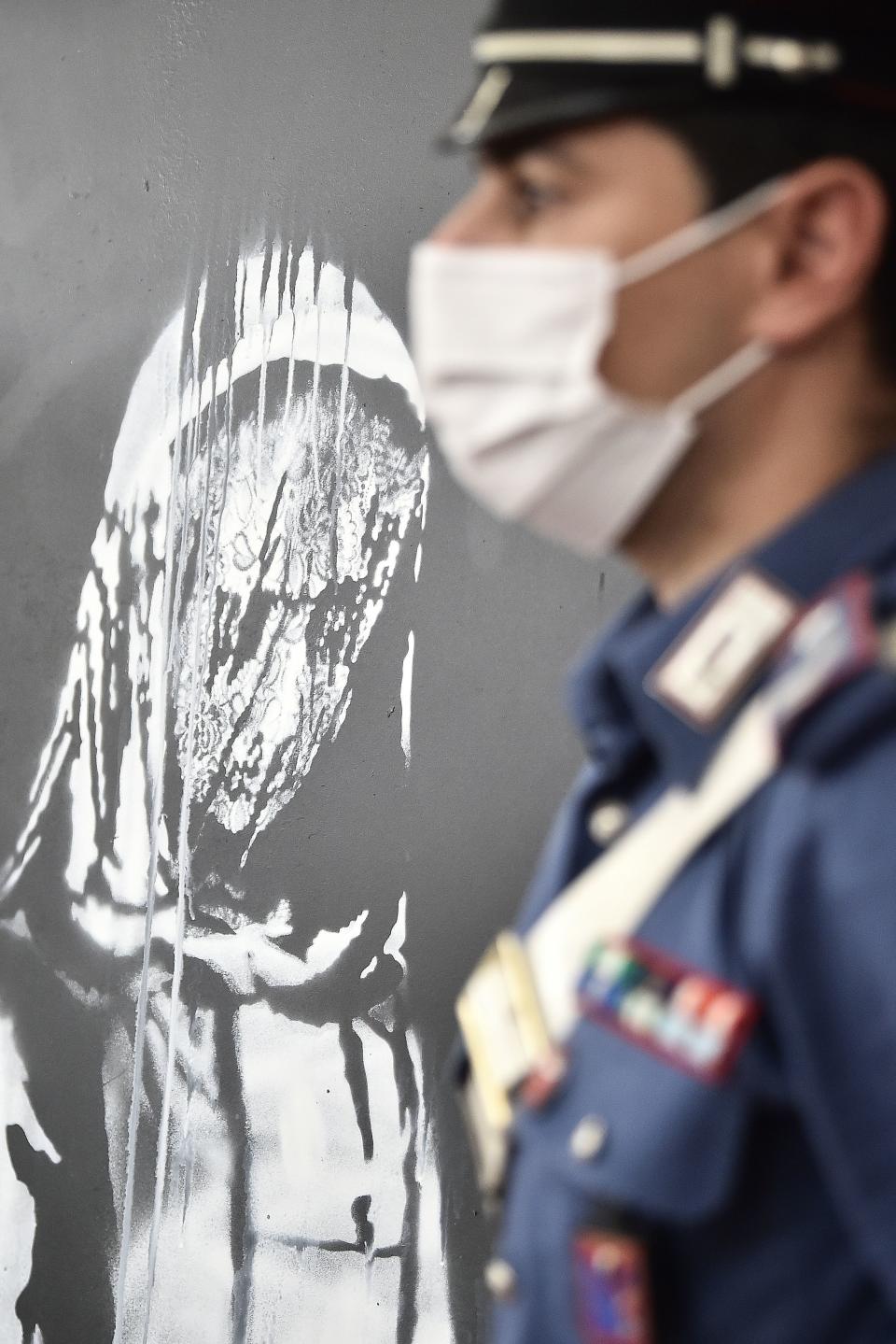 An Italian Carabiniere poses near a piece of art attributed to Banksy, that was stolen at the Bataclan in Paris in 2019, and found in Italy, during a press conference by Italian Carabinieri in L'Aquila on June 11, 2020. - The work was found in an abandoned farmhouse in Abruzzo, l'Aquila prosecutor informed on June 10, 2020. (Photo by Filippo MONTEFORTE / AFP) / RESTRICTED TO EDITORIAL USE - MANDATORY MENTION OF THE ARTIST UPON PUBLICATION - TO ILLUSTRATE THE EVENT AS SPECIFIED IN THE CAPTION (Photo by FILIPPO MONTEFORTE/AFP via Getty Images)