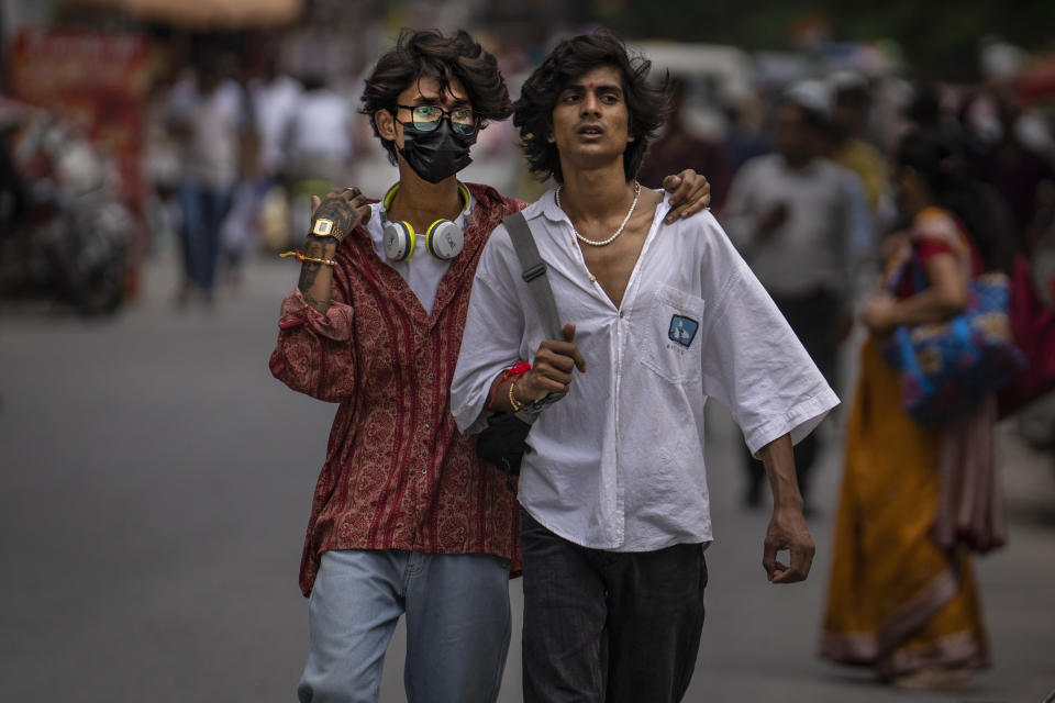 Two boys, one wearing a mask as a precaution against coronavirus walks through a market in New Delhi, India, Thursday, Aug. 11, 2022. The Indian capital reintroduced public mask mandates on Thursday as COVID-19 cases continue to rise across the country. (AP Photo/Altaf Qadri)