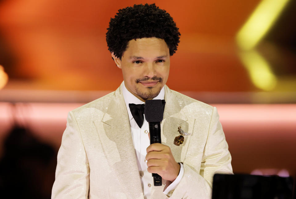 Trevor Noah in a white suit holding a microphone onstage