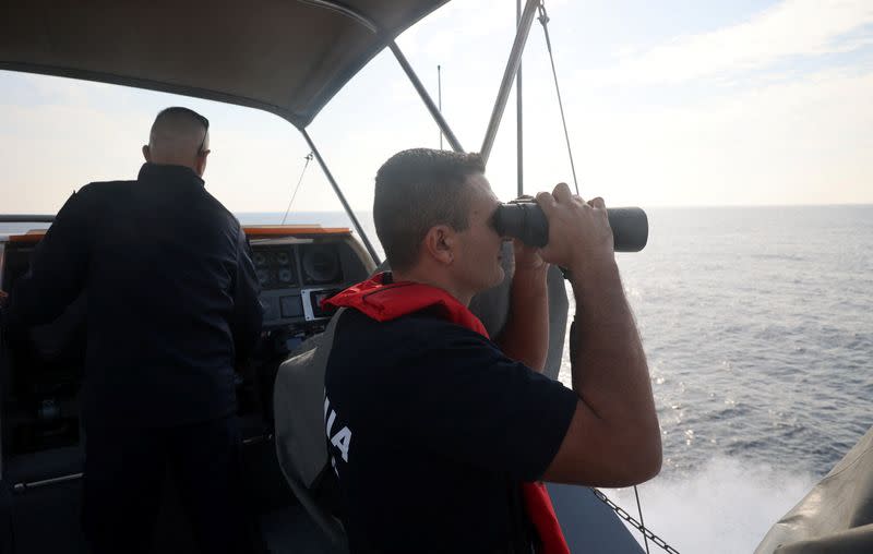 An officer uses binoculars on a Cyprus Port and Marine Police vessel during a patrol in Cape Greco area