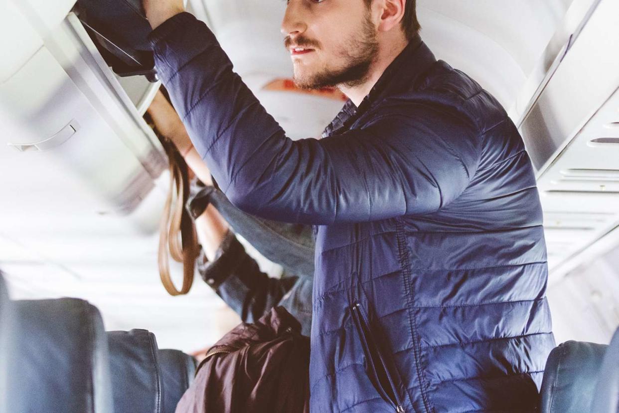 <p>izusek/Getty</p> Man placing a bag in the overhead compartment on the plane