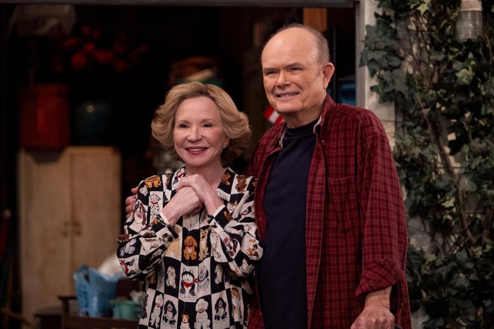 Two actors on a TV set, one in a patterned blouse and the other in a plaid shirt, posing with smiles