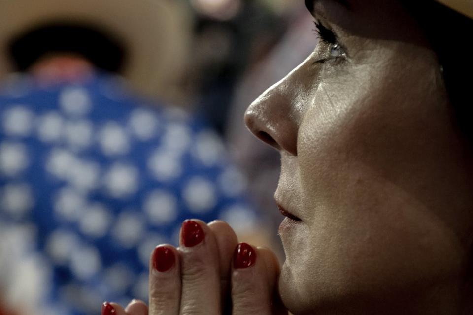 photograph of a woman praying while looking at Donald Trump at the Republican National Convention 2024