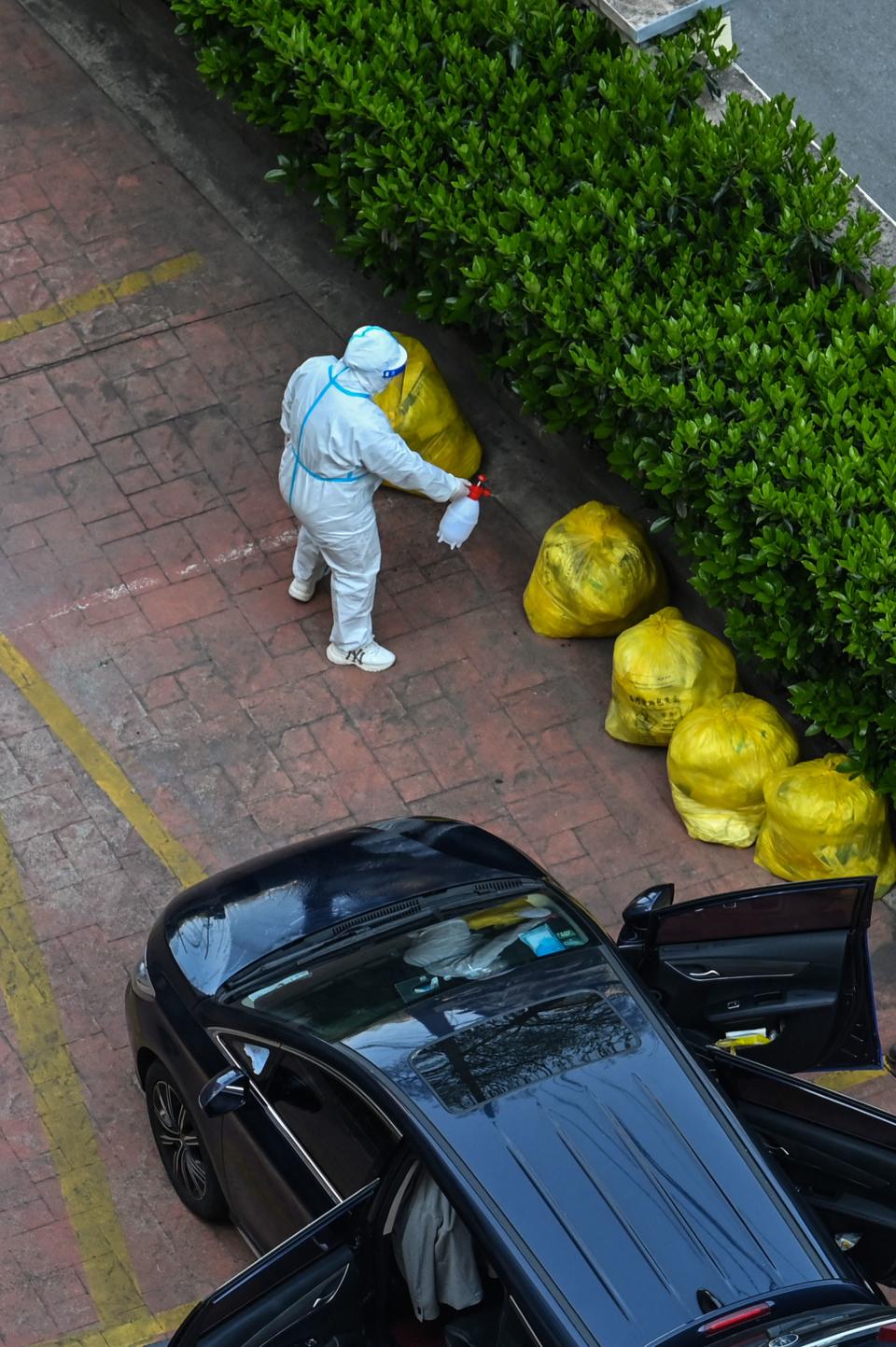 A worker wearing protective gear sprays disinfectant on bags next to a building in Shanghai on April 3. Source: Getty