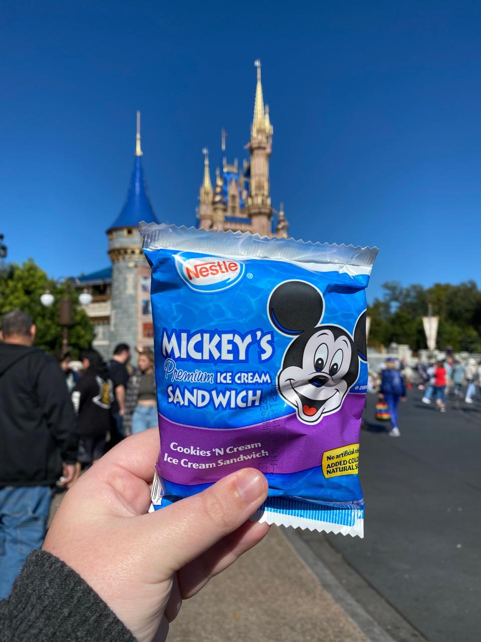 hand holding a package containing mickey ice cream sandwich in front of the castle at disney world