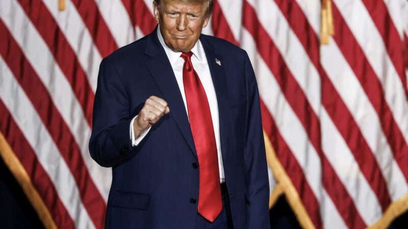 Trump stands in front of an American flag