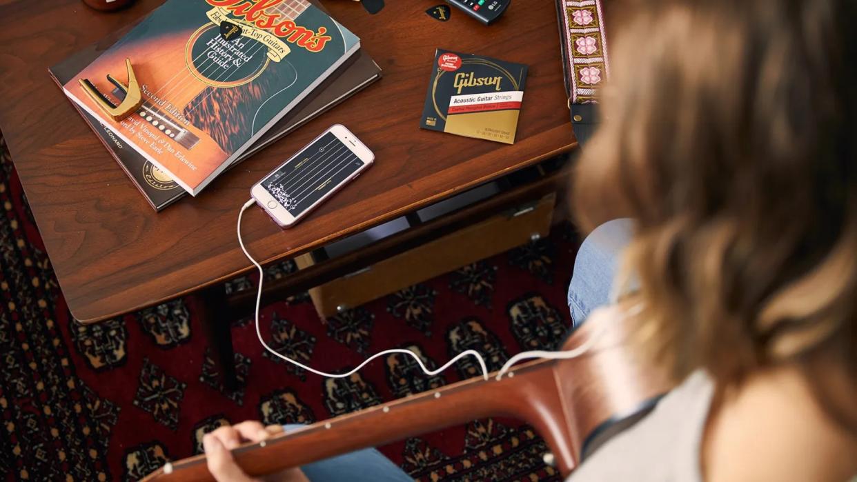  Woman plays an acoustic guitar using the Gibson lessons app. 