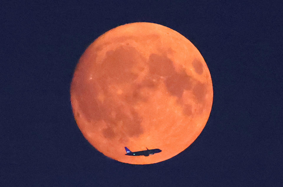 Ein Flugzeug fliegt vor dem Mond vorbei, mit einem roten Schimmer, der auf Rauchpartikel zurückzuführen ist, die durch Waldbrände in Nordamerika in die obere Atmosphäre getragen wurden, einen Tag vor dem Vollmond, wie vom Parliament Hill in London, Großbritannien, am 18. August aus gesehen werden kann. 2024. / Bildnachweis: Toby Melville/REUTERS