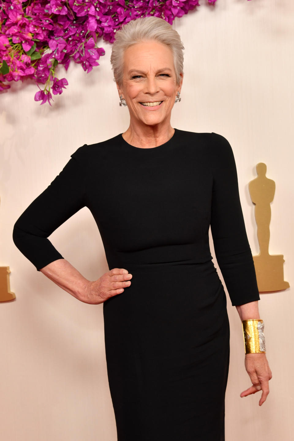 Jamie Lee Curtis poses in a long-sleeved black gown with a gold cuff bracelet