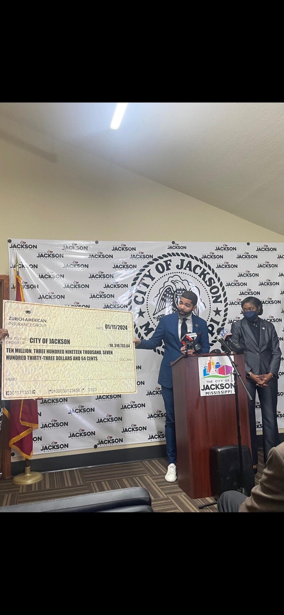 Jackson Mayor Chokwe Antar Lumumba, along with City Attorney Catoria Martin, hold up a symbolic $10.3 million check from Zurich-American Insurance Group at mayor's press conference Thursday at the Real-Time Command Center.