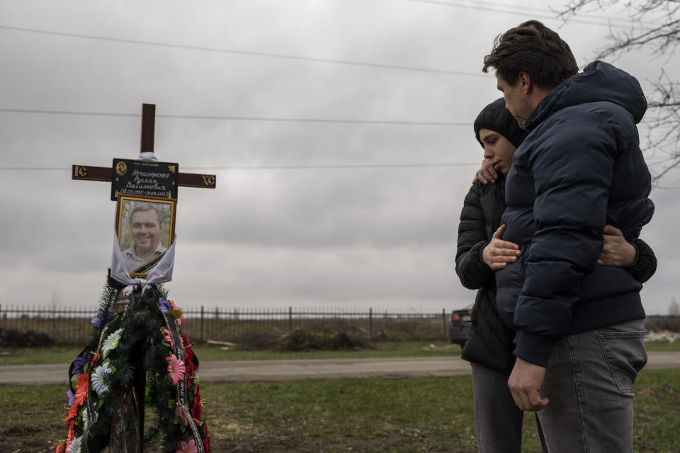 Yura Nechyporenko abraza a su tío Andriy Nechyporenko ante la tumba de su padre, Ruslan Nechyporenko, en el cementerio de Bucha, a las afueras de Kiev, Ucrania, el jueves 21 de abril de 2022. El joven sobrevivió a un intento de ejecución de soldados rusos, mientras que su padre murió, y ahora la familia pide justicia. (AP Foto/Petros Giannakouris)