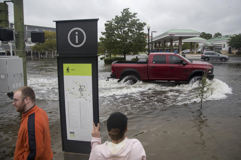 Emily Enyeart throws up a peace sign to a truck as it successfully passes through the flooding on West Olney Road in Norfolk, Va., on Friday, Sept. 6, 2019. (Sarah Holm/The Virginian-Pilot via AP)