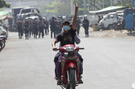 A protester on a motorbike flashes the three-fingered salute while soldiers and police take position to disperse protesters on one of the main roads in Mandalay, Myanmar, Friday, Feb. 26, 2021. Security forces in Myanmar's largest city Yangon on Friday fired warning shots and beat truncheons against their shields while moving to disperse more than 1,000 anti-coup protesters. (AP Photo)