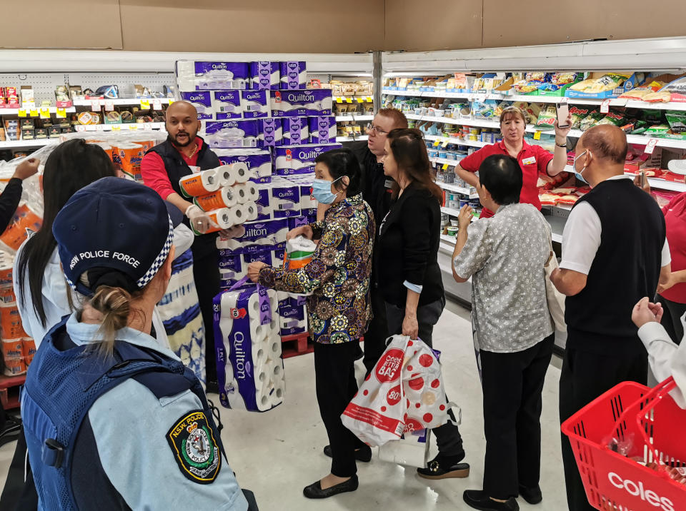 People receiving toilet paper, paper towel and pasta as a police officer watches on at Coles Supermarket, Epping in Sydney. Source: AAP