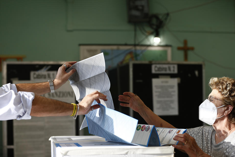 A woman receives her ballot at a polling station, in Rome, Sunday, Oct. 3, 2021. Millions of people in Italy started voting Sunday for new mayors, including in Rome and Milan, in an election widely seen as a test of political alliances before nationwide balloting just over a year away. (Cecilia Fabiano/LaPresse via AP)