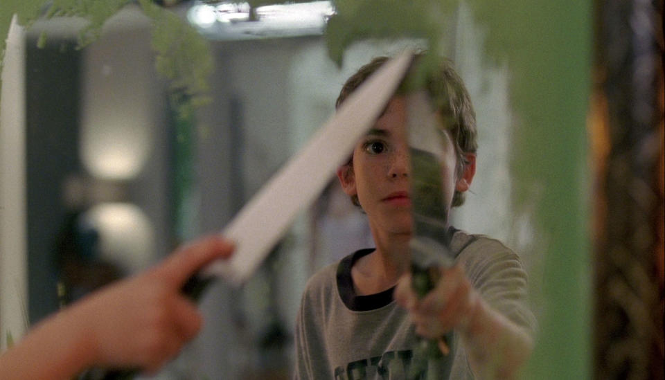 A little boy holding a knife to a mirror